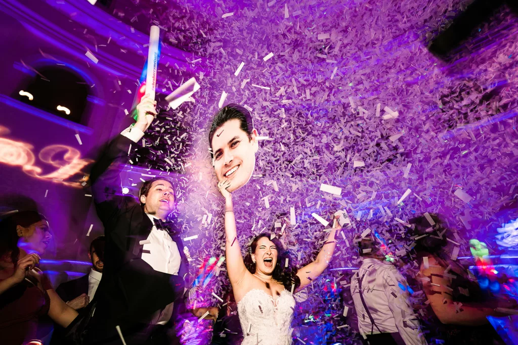 A couple dances while the air is filled with confetti surrounded by guests.