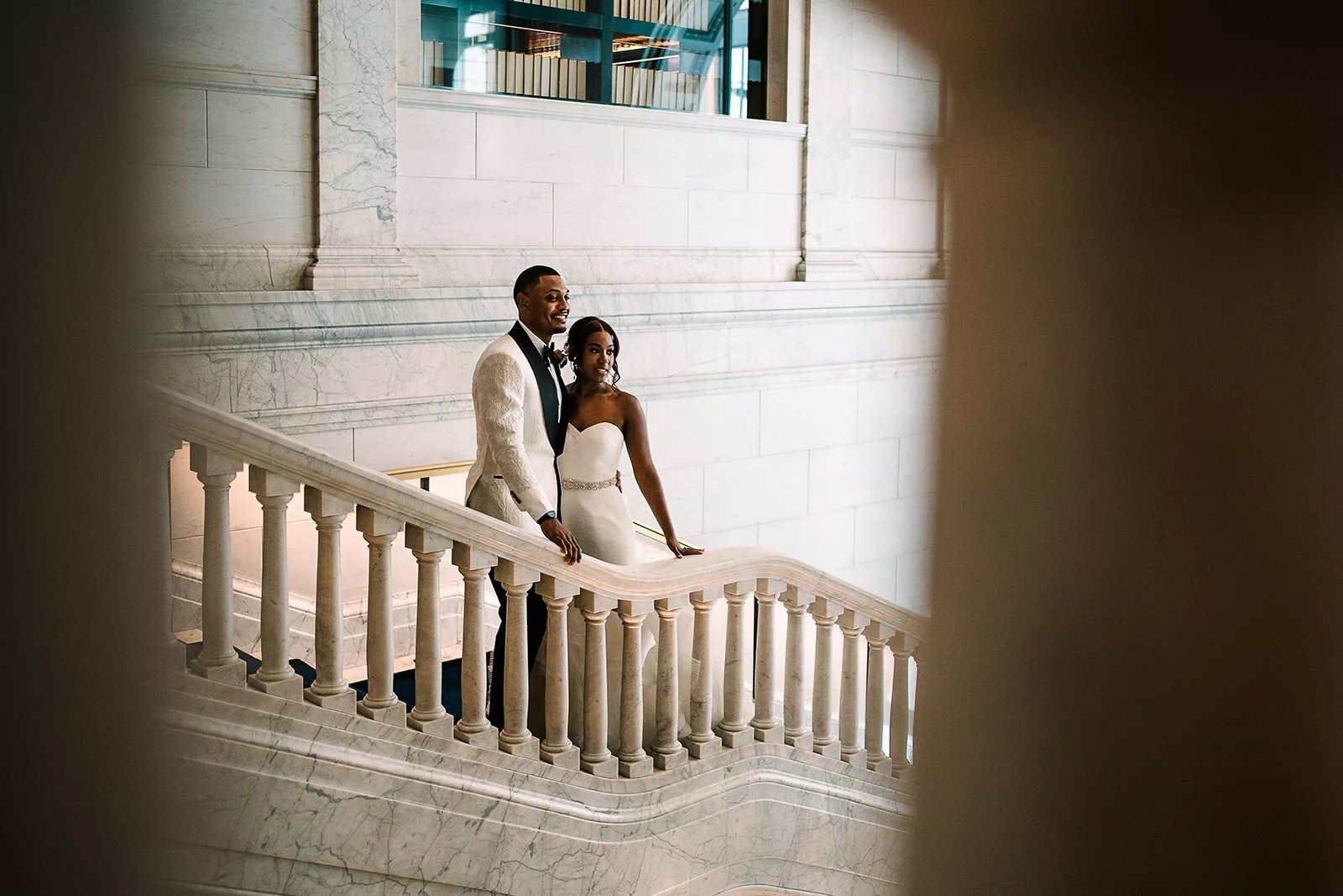 A captivating and elegant image of a couple's wedding celebration, featuring a breathtaking staircase as the backdrop, with the couple holding hands and sharing a tender moment